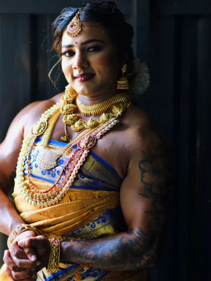 A moment of quiet confidence during a photoshoot. The intricate gold jewelry and silk saree contrast with the visible strength of my shoulders and arms, a core part of my identity.