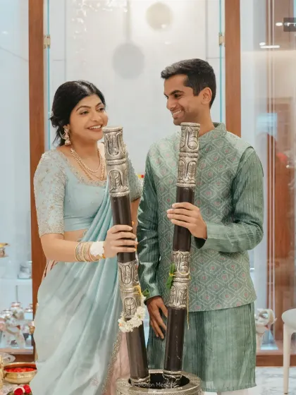 A couple holds traditional silver pillars, participating in a pre-wedding ritual at home that honors their family customs.