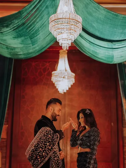 The couple shares a delicate, intimate moment under a grand crystal chandelier, a perfect blend of romance and opulent decor during their reception.