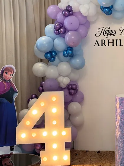 Anna stands by the glowing number '4' marquee light, part of the enchanting Frozen birthday setup.