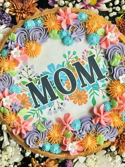 A detailed shot of the "MOM" chocolate tart, focusing on the intricate and colorful buttercream piping work that borders the edible printed design.