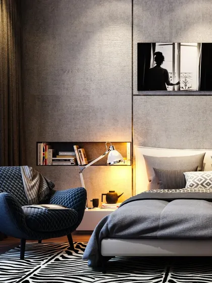 A cozy bedroom corner with a quilted armchair, a zebra-print rug, and a built-in niche for books. The dark, textured walls and soft lighting create an intimate and moody atmosphere.