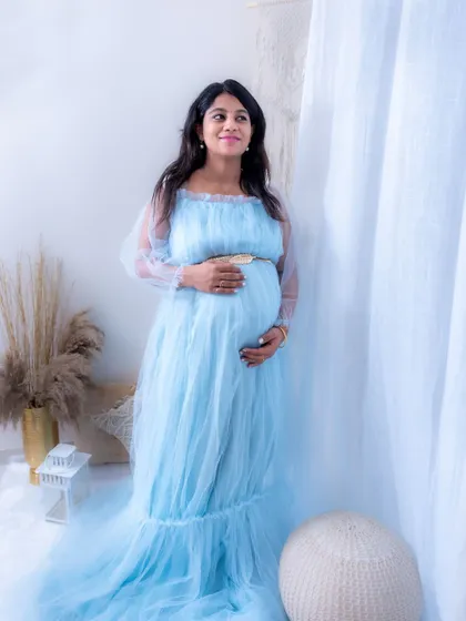 A peaceful and serene lifestyle portrait from our studio. The mom-to-be is wearing a light blue gown and looking thoughtfully out a window.