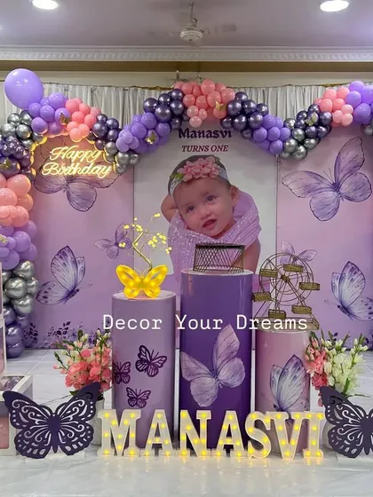 A beautiful butterfly theme for a first birthday. This elegant setup includes a purple and pink balloon arch, a custom photo backdrop, marquee letters, and decorative butterfly cutouts.