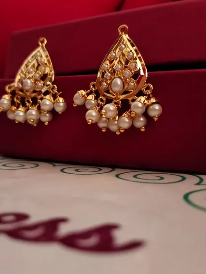 The "Kali" gold-plated Jadau earrings feature a classic teardrop shape with delicate pearl clusters. This product shot highlights their timeless elegance against our signature red gift box.
