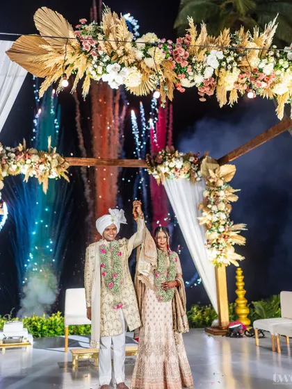 A spectacular night varmala at a Goa destination wedding. The couple celebrates under a beautifully lit mandap with fireworks in the background.