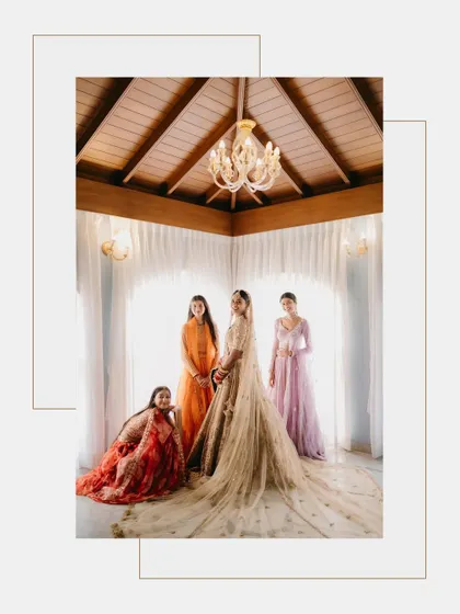 A beautifully composed portrait of a bride with her bridesmaids, all elegantly dressed, inside a room with a high wooden ceiling and chandelier.