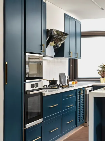 A closer look at the functional side of the blue kitchen. We integrated the oven and microwave into a tall unit for a seamless look and ergonomic use. The slim brass handles add a touch of elegance to the shaker-style cabinets.