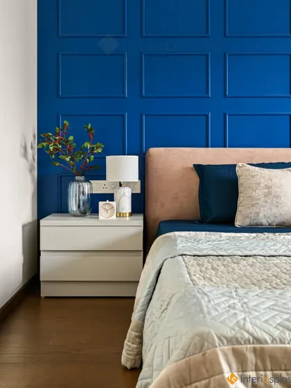 A close-up of the bedside in the blue room, showing the white nightstand and modern lamp against the dramatic backdrop of the panelled wall.