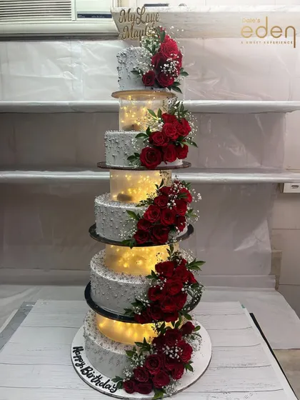 A towering statement of celebration. This multi-tiered cake with separators is illuminated from within and adorned with clusters of red roses, creating a truly spectacular display for a grand event.
