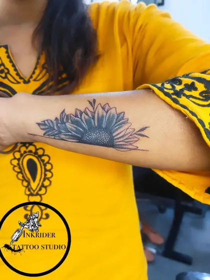 A black and grey sunflower tattoo on the forearm. Floral designs like this are a popular choice for cover-ups, offering great flexibility in shape and shading.
