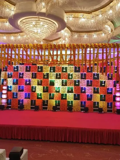 A vibrant and traditional Sangeet stage in a banquet hall. The backdrop features a colorful checkerboard pattern with marigold details, creating a perfect setting for musical performances.