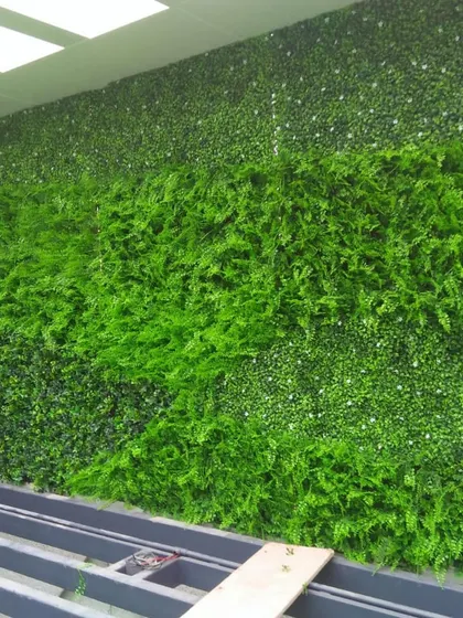 A close-up of a dense, textured artificial green wall, showing the variety of leaf shapes and shades used to create a realistic look.