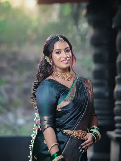 A smiling bride, confident and radiant in her dark green saree and traditional gold jewelry.