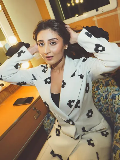 Dhvani Bhanushali in a white suit with black floral print, getting ready in a vanity room.