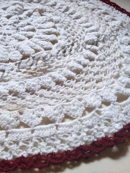 A close-up shot of a large, intricate white doily with a rich maroon border, showing the detailed texture of the stitches.