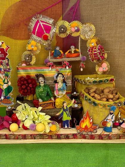 This hamper captures all the colorful vibes of Lohri. It features a decorated platter with figurines, a miniature swing, and jute bags filled with peanuts and other festive treats.