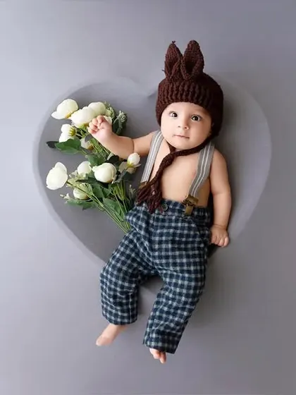 The same baby boy in a bunny-ear hat holds a small bouquet of white flowers.
