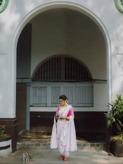 A full-length portrait of a Maharashtrian bride, looking elegant and poised in an arched doorway.
