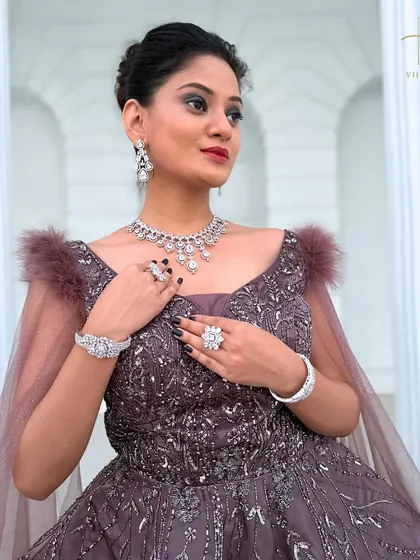 A close-up on the bodice of the mauve gown, showing the intricate beadwork and feather shoulder details.