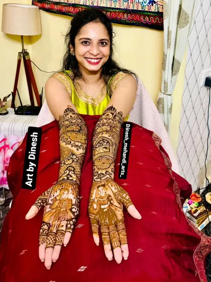 A happy bride showcasing her full-arm portrait mehendi. The design features detailed figures of a bride and groom, a perfect example of my signature work.