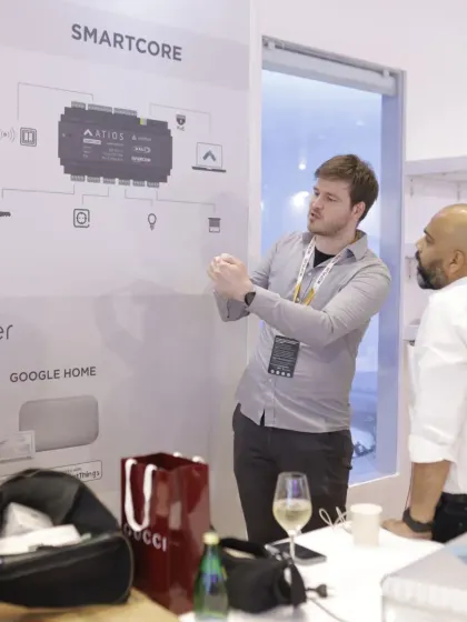 An exhibitor presents a diagram of a 'SmartCore' system, explaining its integration capabilities with platforms like Google Home to interested attendees.