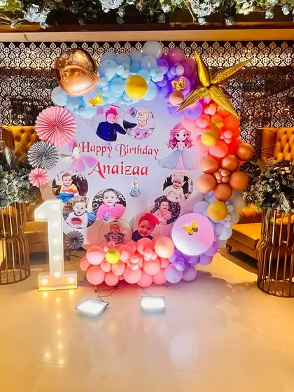 A fairy-themed first birthday with a photo collage backdrop, surrounded by a colorful balloon ring and fairy character cutouts.