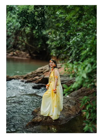 A beautiful portrait of a bride during her Haldi photoshoot, standing by a stream in her yellow attire.