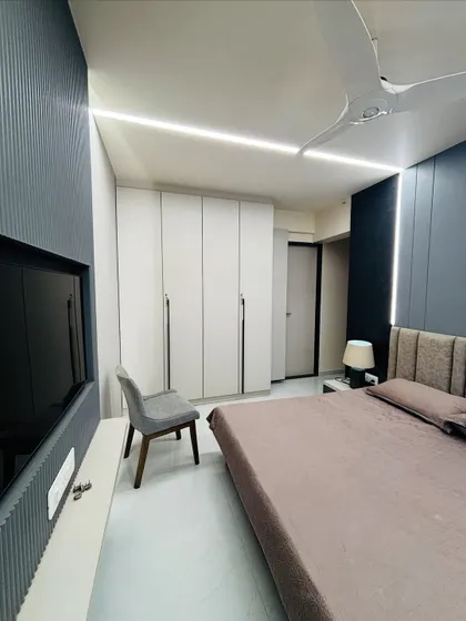 This shot shows the relationship between the TV unit, wardrobe, and bed. The floor-to-ceiling white wardrobe makes the room feel spacious, while the dark accent walls add depth.
