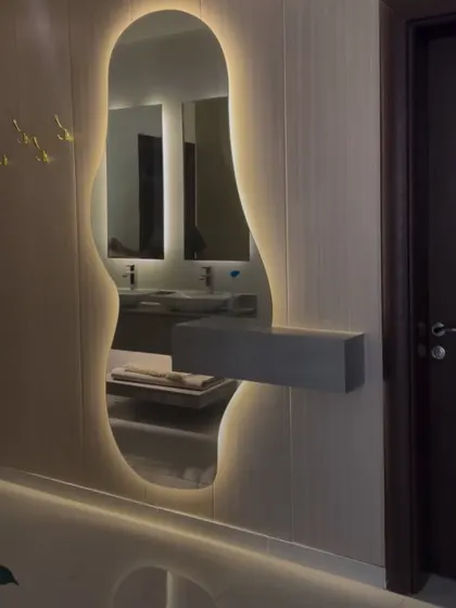 This free-form, organically shaped dressing mirror with backlighting adds a soft and modern touch to the room. The small floating shelf is perfect for essential items.