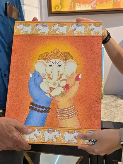 A client receiving their custom Ganesha painting. This piece, rendered in a traditional style, depicts the deity being held in loving hands, symbolizing protection and care.