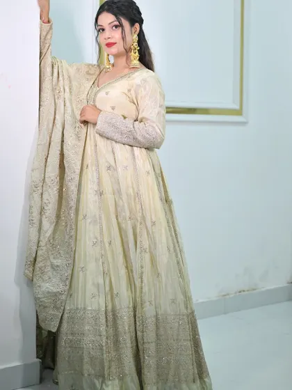 A model posing against a white wall in the ivory anarkali gown, highlighting the elegant V-neck and embellished sleeves.