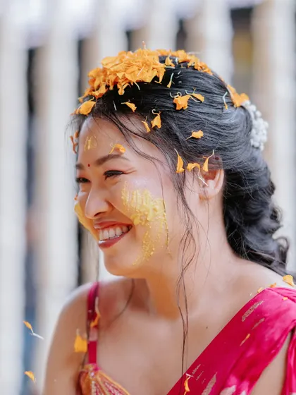 The bride's happy face, covered in turmeric paste and flower petals, captures the essence of the Haldi ceremony.