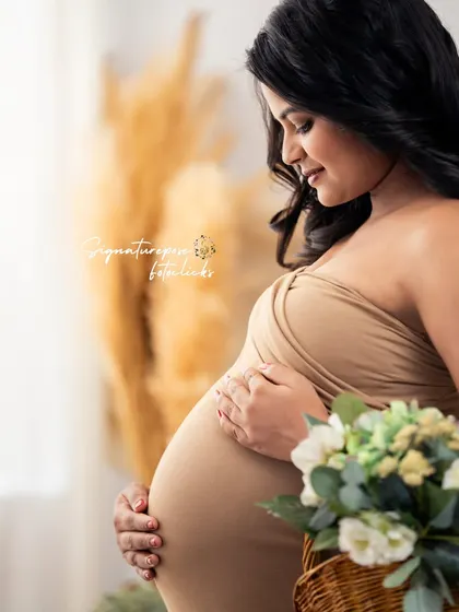 A close-up shot focusing on the tender moment of cradling the bump, with a soft bouquet adding a touch of color.