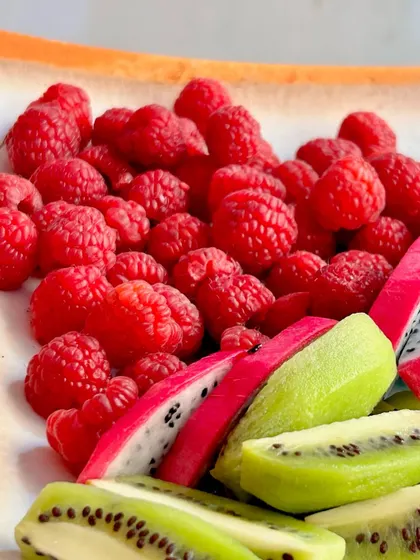 A platter of fresh raspberries, kiwi, and dragon fruit, showcasing a mix of premium and exotic fruits.