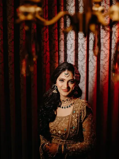 A stunning bridal portrait against a rich, red curtain. The dramatic lighting and her confident gaze create a powerful and glamorous image.