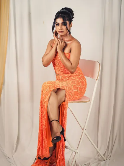 This seated pose reveals the beautiful drape of the orange gown and its alluring slit, making it a dynamic piece for any occasion.