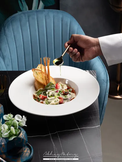 This image is a perfect example of my work. It shows the final, beautifully lit and styled dish, but also includes the chef's hand adding the finishing touch, giving a peek into the creation process.