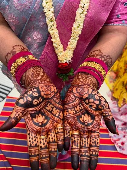 A beautiful shot of mehendi-adorned hands with traditional bangles and a flower garland.
