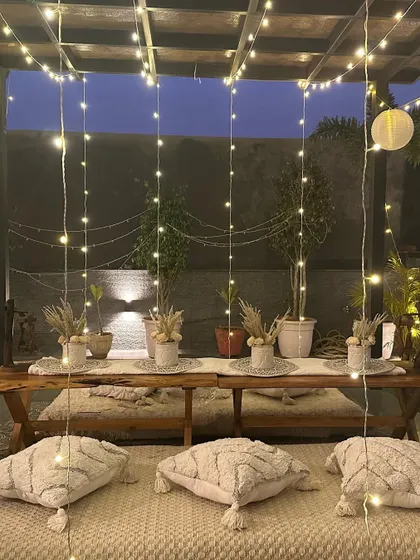 The full view of the boho-chic low seating arrangement. The combination of the wooden table, plush cushions, and a curtain of fairy lights creates a magical and inviting space.