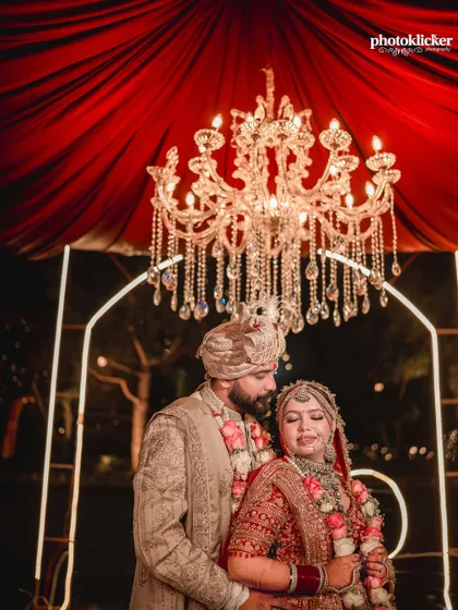 An intimate shot of the couple during their Jaimala ceremony, framed by a magnificent crystal chandelier that adds to the grandeur of the moment.