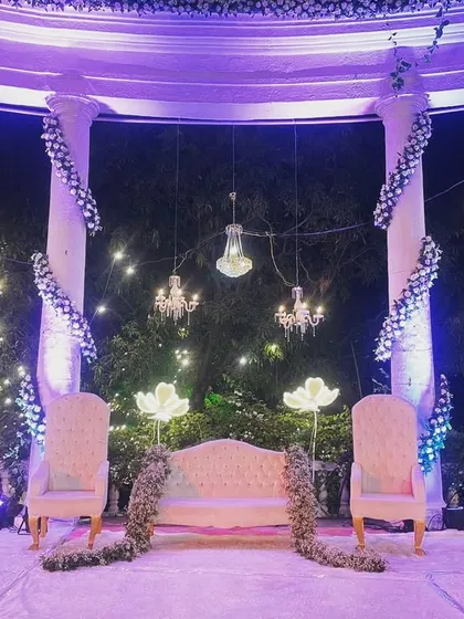A dreamy reception stage setup featuring elegant white seating for the couple. We used hanging chandeliers and illuminated floral props to create a whimsical and romantic atmosphere.