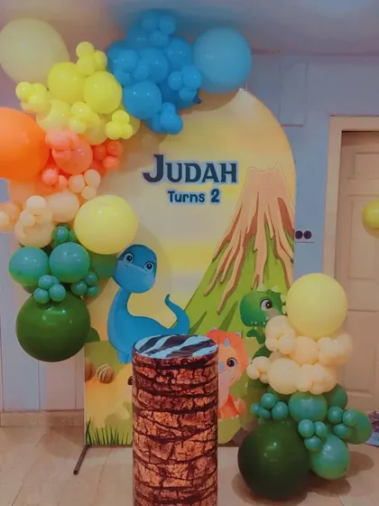 A cute cartoon dinosaur theme featuring a volcano backdrop and a colorful balloon garland.