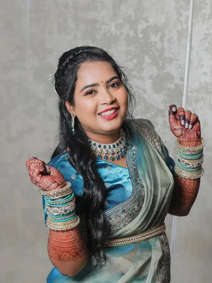 A close-up of the bride, smiling and dancing with her hands up. This shot captures her happiness and the intricate details of her mehndi, jewelry, and shimmering saree.
