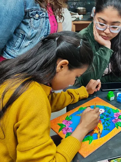 A student painting her finished clay mural. This final step brings the 3D artwork to life with color and personality.