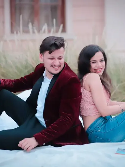 A relaxed and happy moment from a creative pre-wedding shoot. The couple is sitting back-to-back on a picnic blanket, sharing a smile in a beautifully styled outdoor setting.