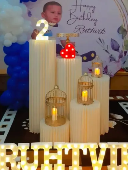 A Boss Baby themed second birthday party. The setup includes a circular backdrop with a photo, balloon columns, and decorative props like candle-lit birdcages.