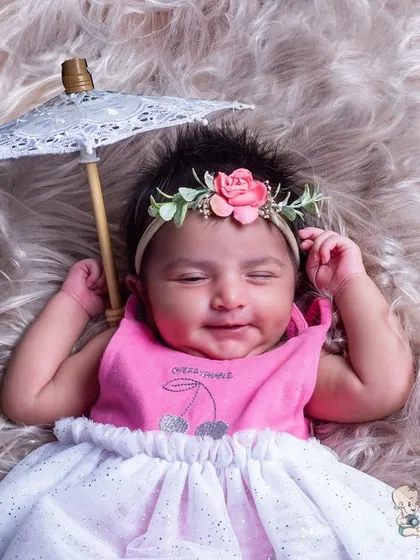 A happy baby girl with a beautiful smile, lying on a soft fur blanket and holding a tiny lace umbrella. This simple and sweet setup is perfect for capturing your baby's emerging personality.