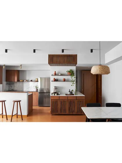 This open-plan space includes a kitchen with a breakfast bar and custom wood cabinetry. The slatted wood detail on the island adds texture and a sense of rhythm to the design.