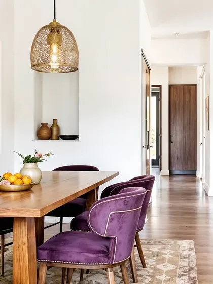 An open-concept dining area where bold purple chairs are paired with a warm wood table and floors. The design feels modern, welcoming, and full of personality.